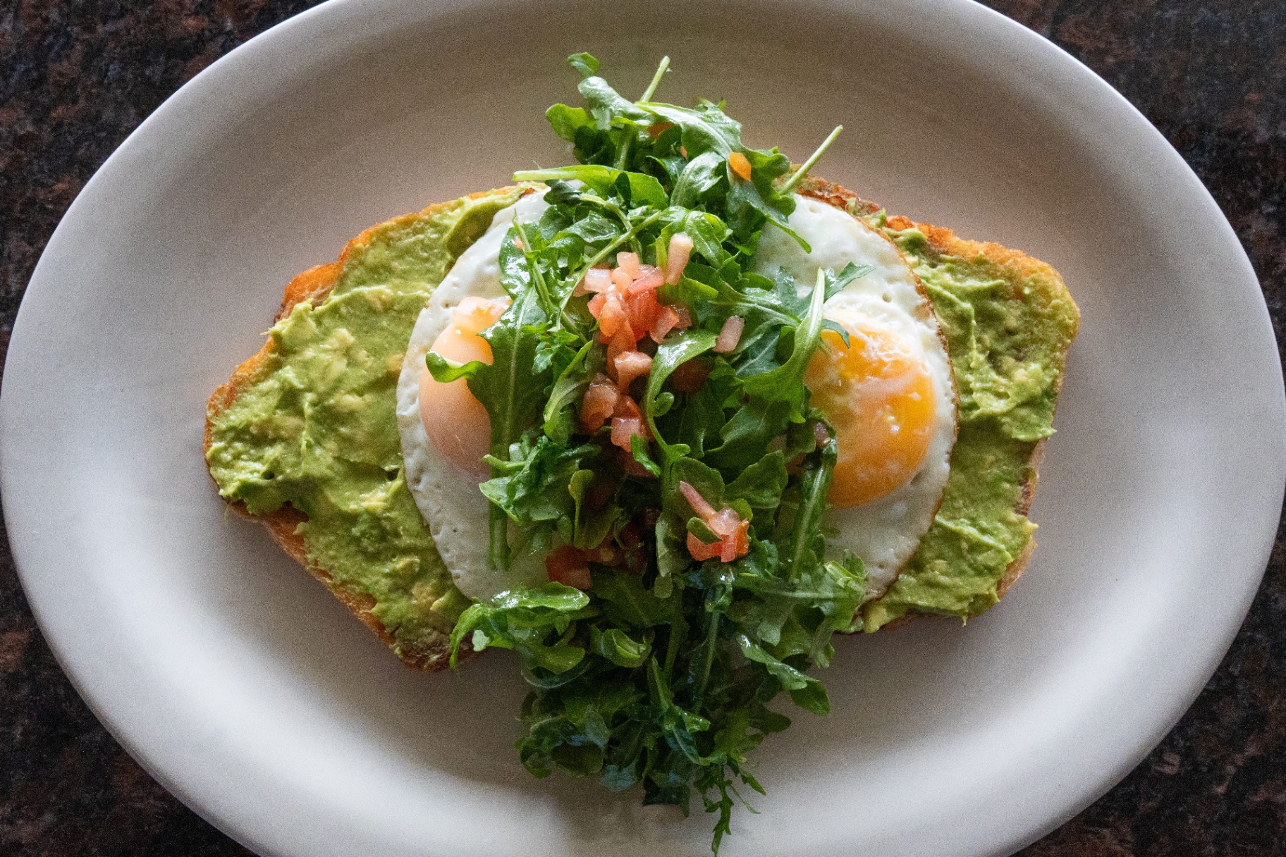 Avocado toast with sunny-side eggs, arugula, and pico de gallo