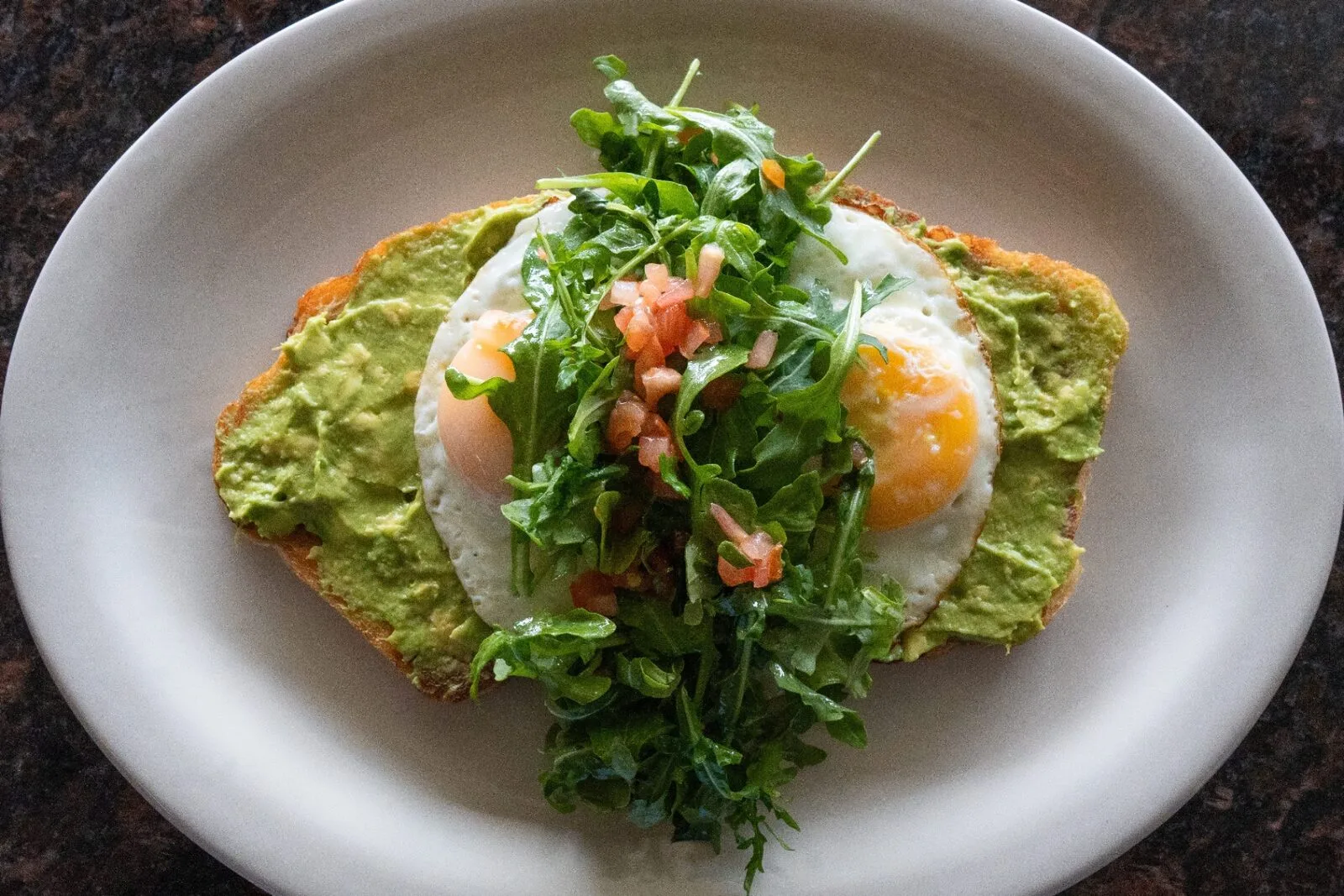 Avocado toast with sunny-side eggs, arugula, and pico de gallo