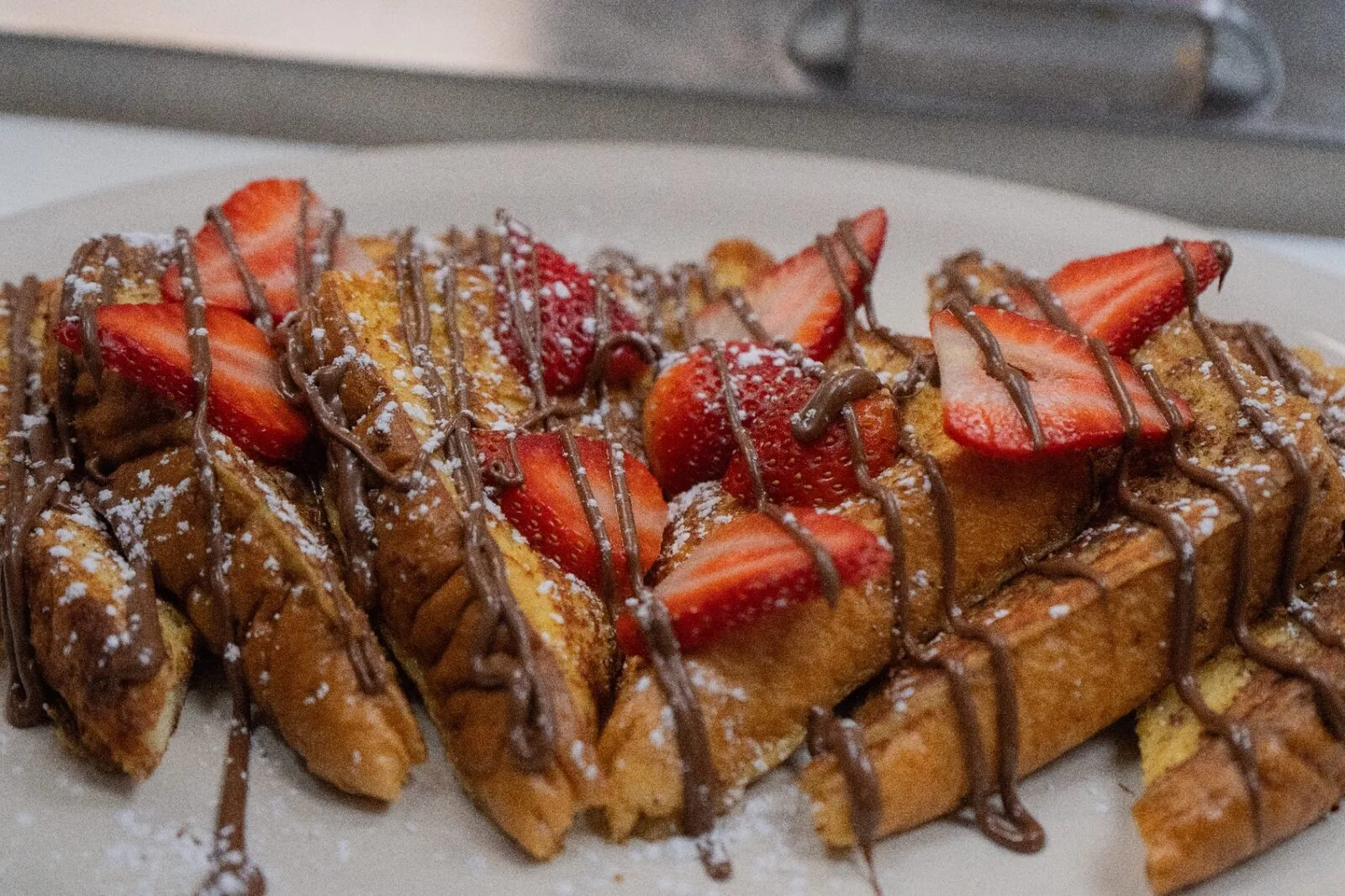 French toast with strawberries, Nutella drizzle, and powdered sugar